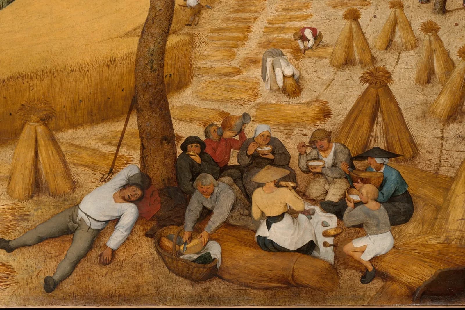 Detail of The Harvesters by Pieter Bruegel the Elder: farm workers resting beneath a pear tree beside sheaves of wheat.