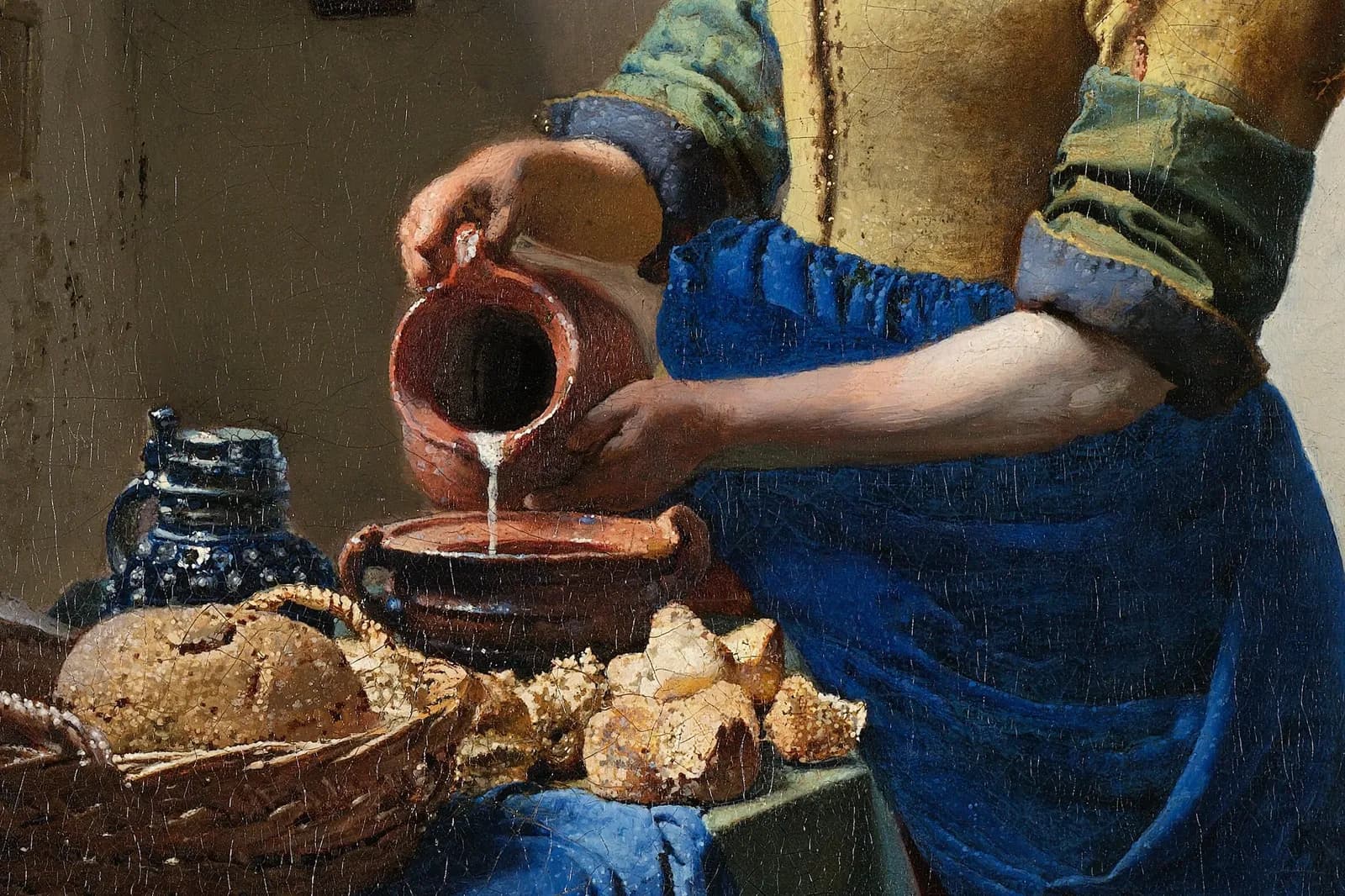 Detail of The Milkmaid by Johannes Vermeer: a kitchen maid pouring milk into a bowl beside a basket of bread.